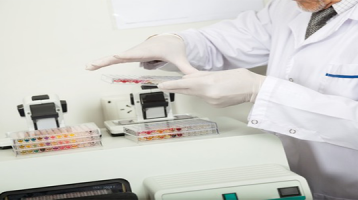 Scientist Examining 96-Well Plate Near Plate Reader